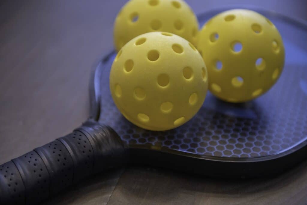 Close-up of yellow pickleball balls on black paddle with honeycomb pattern